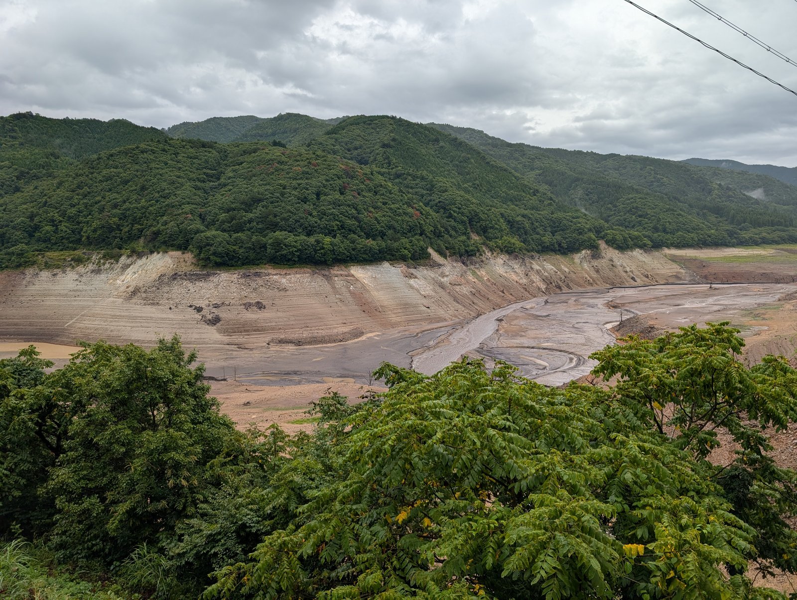 荘川桜公園の湖畔から見た御母衣湖。水位が下がり、岸の斜面が階段状に現れている（2026-08-27 撮影）