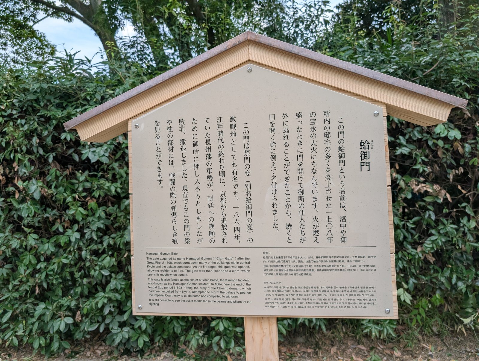 現地の説明板「蛤御門」。日本語・英語・中国語・韓国語の四か国語で、門の名の由来と禁門の変を記す（2026-08-22 撮影）