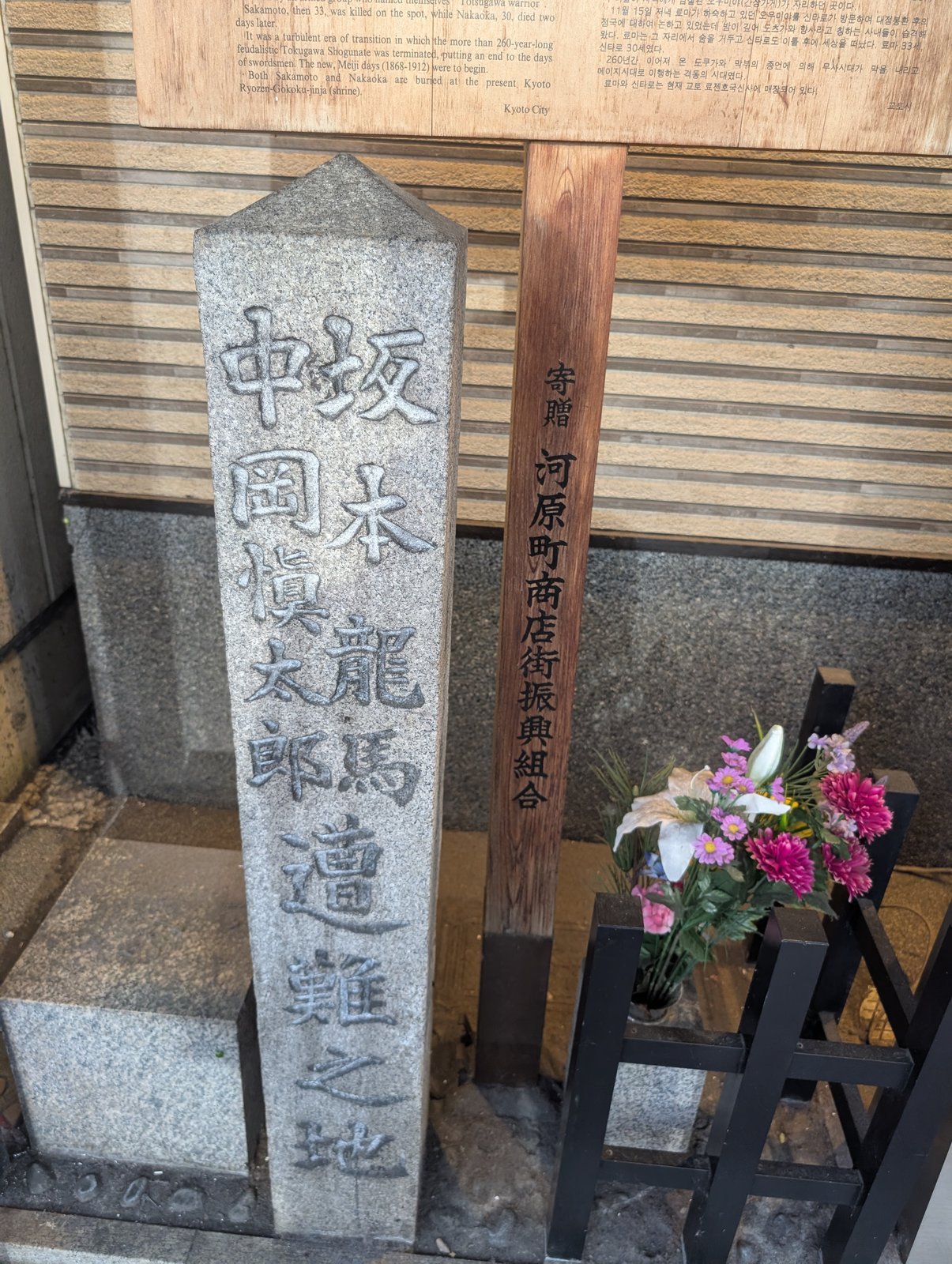河原町通に面した歩道に立つ「坂本龍馬 中岡慎太郎 遭難之地」の石標。花が供えられている。右の木の柱には「寄贈 河原町商店街振興組合」とある（2026-08-22 撮影）